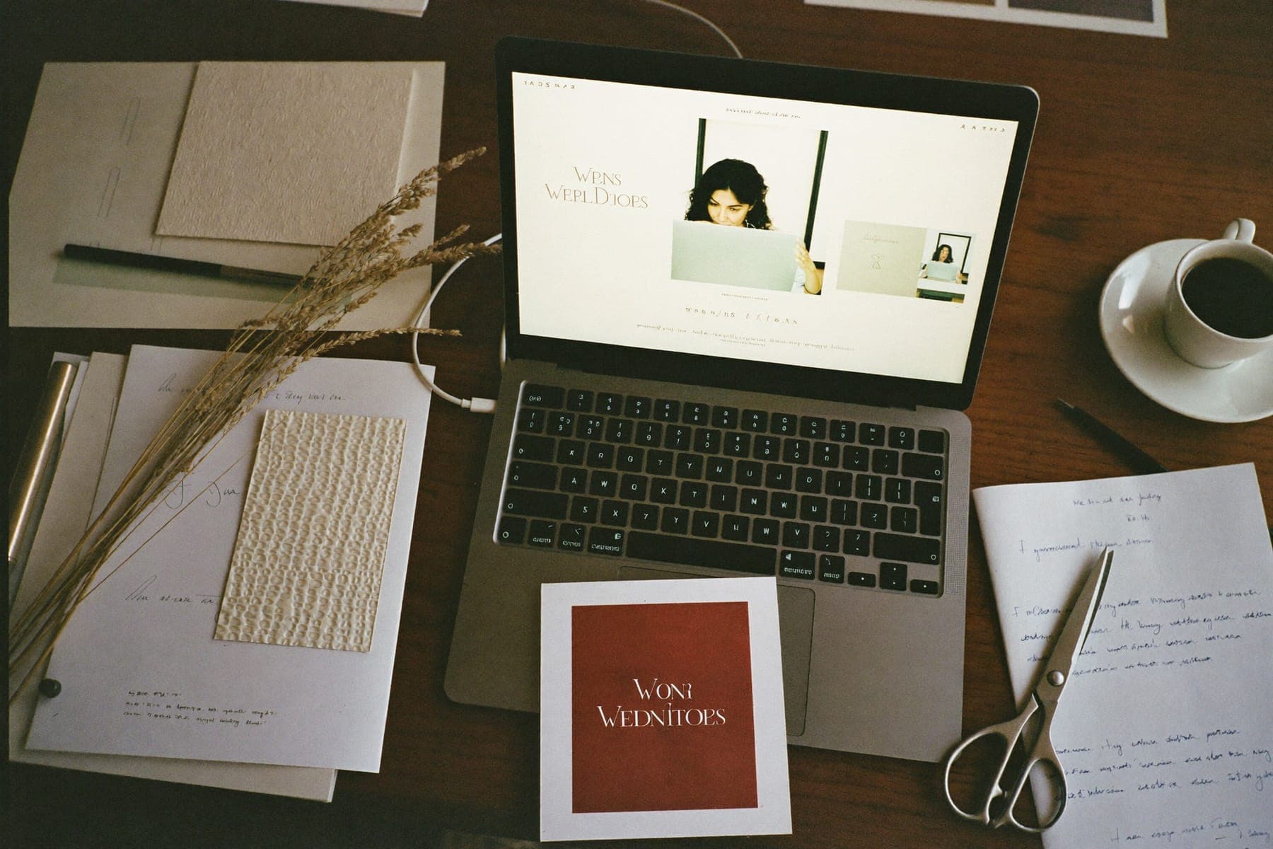 Mesa de estudio diseñando una invitación de boda digital: portátil, muestras de papel y flores secas